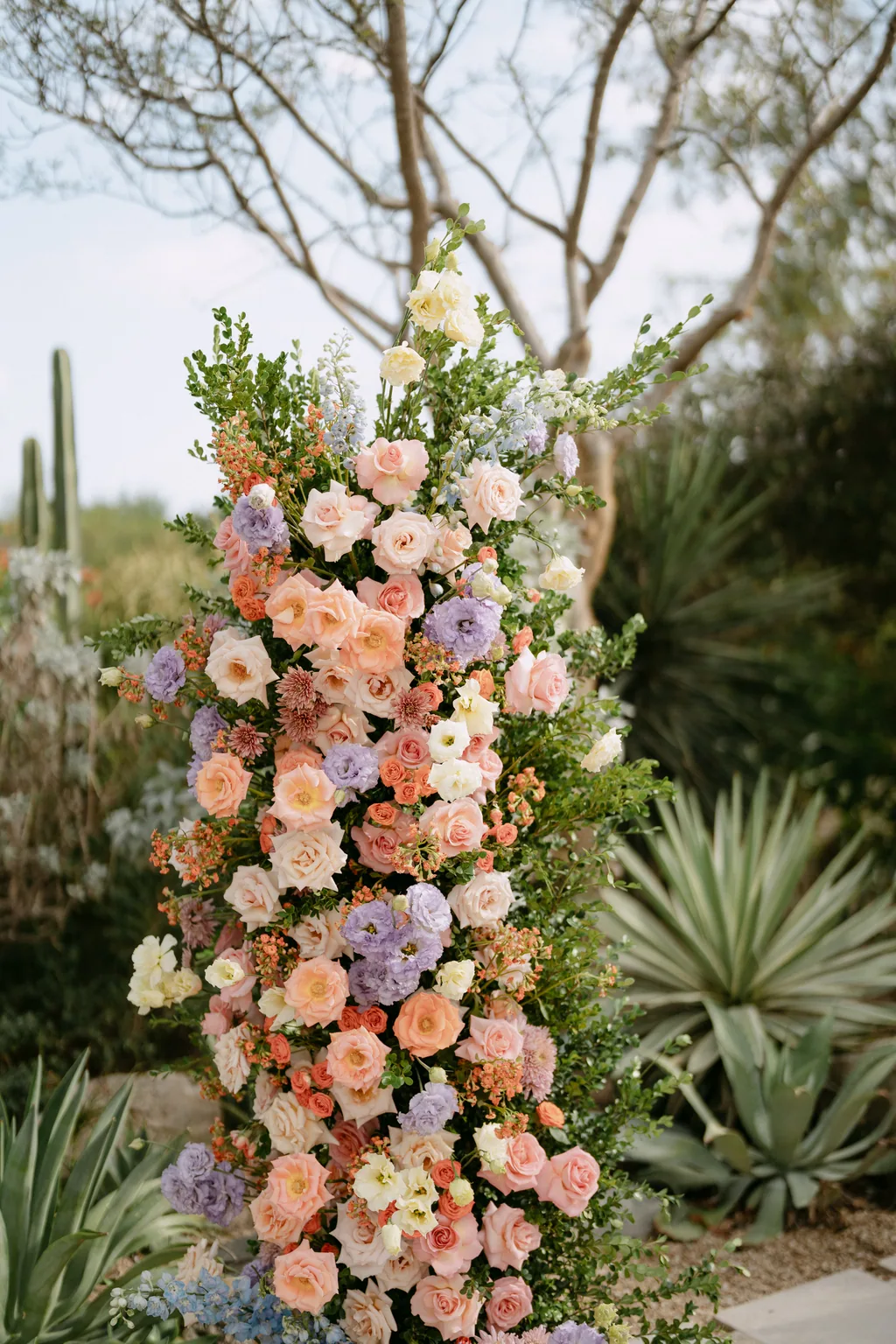 The ceremony flower column in peach, lilac and blue, set among the agaves