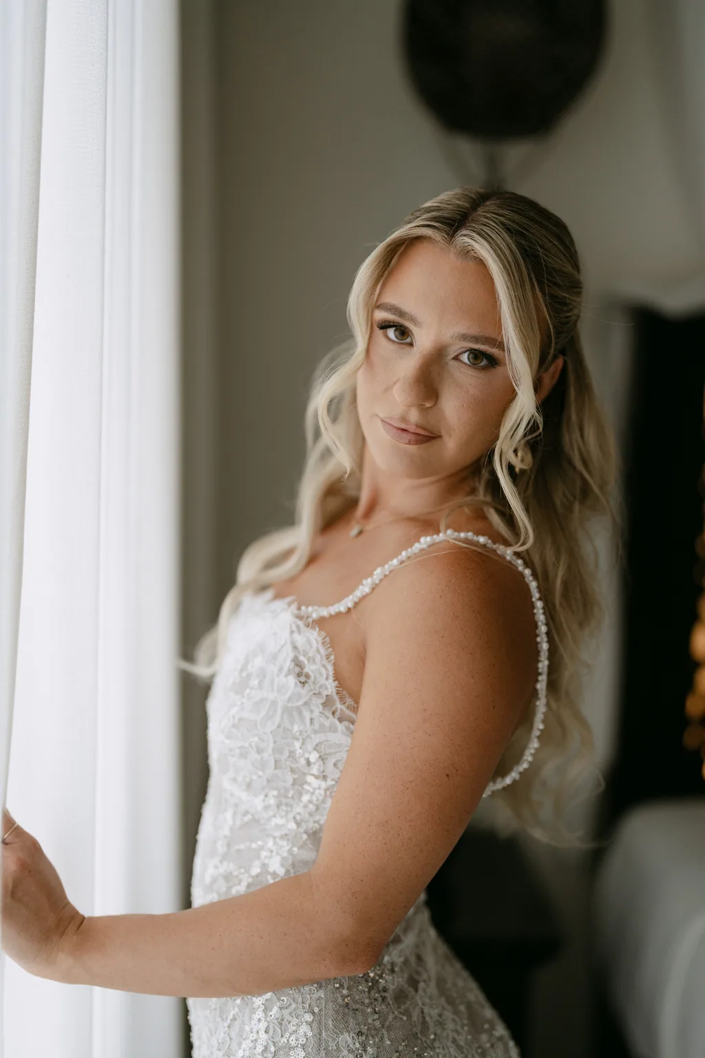 Bailey by the window in her wedding dress, light coming through the curtain