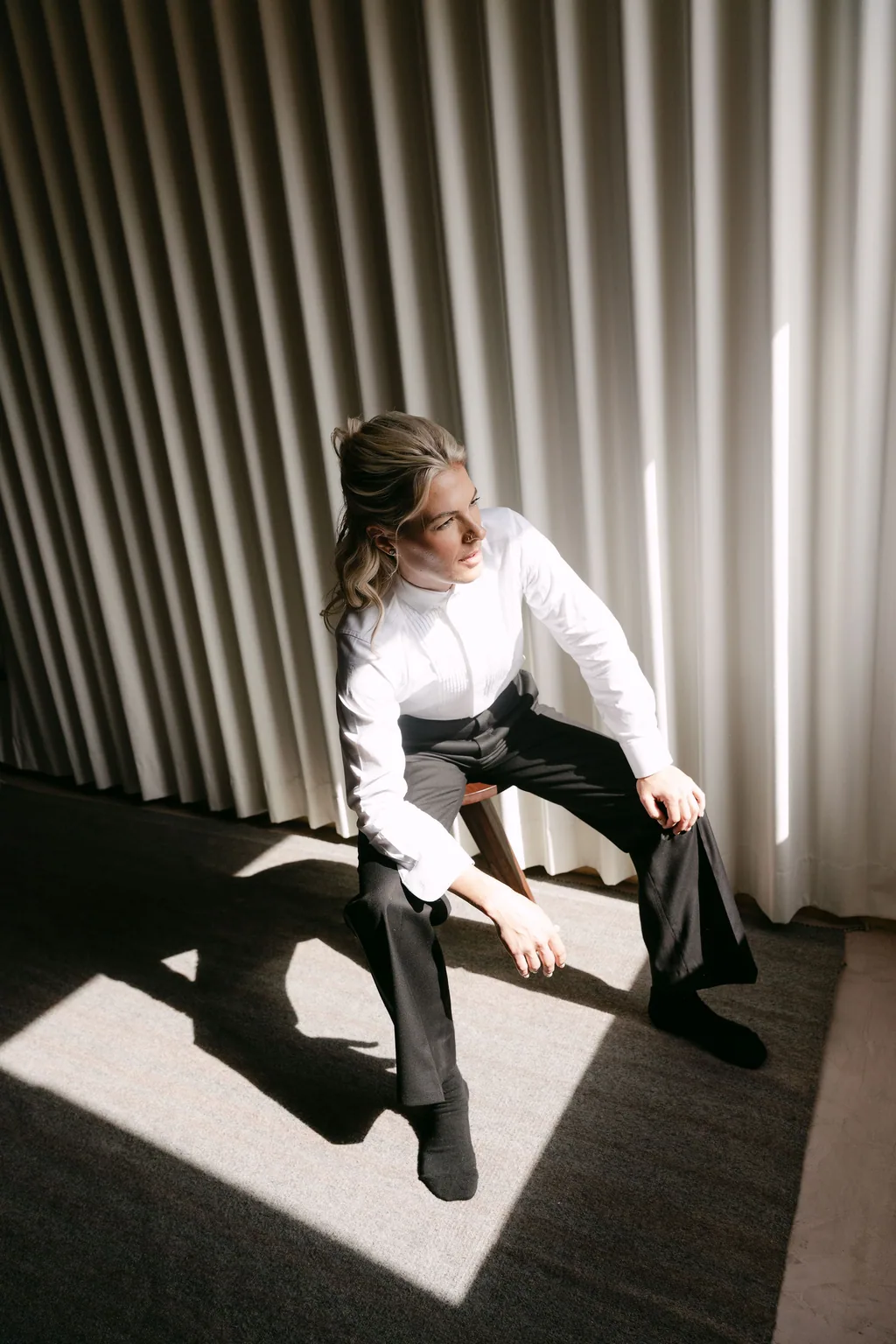 The bride in the tuxedo seated in a shaft of light before the ceremony