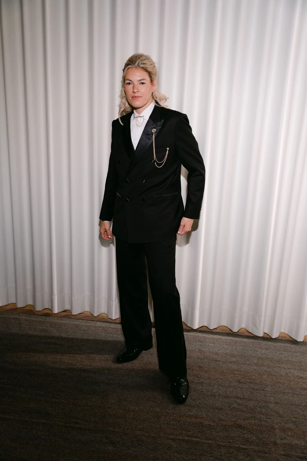 The bride in the black tuxedo, full length against the curtain