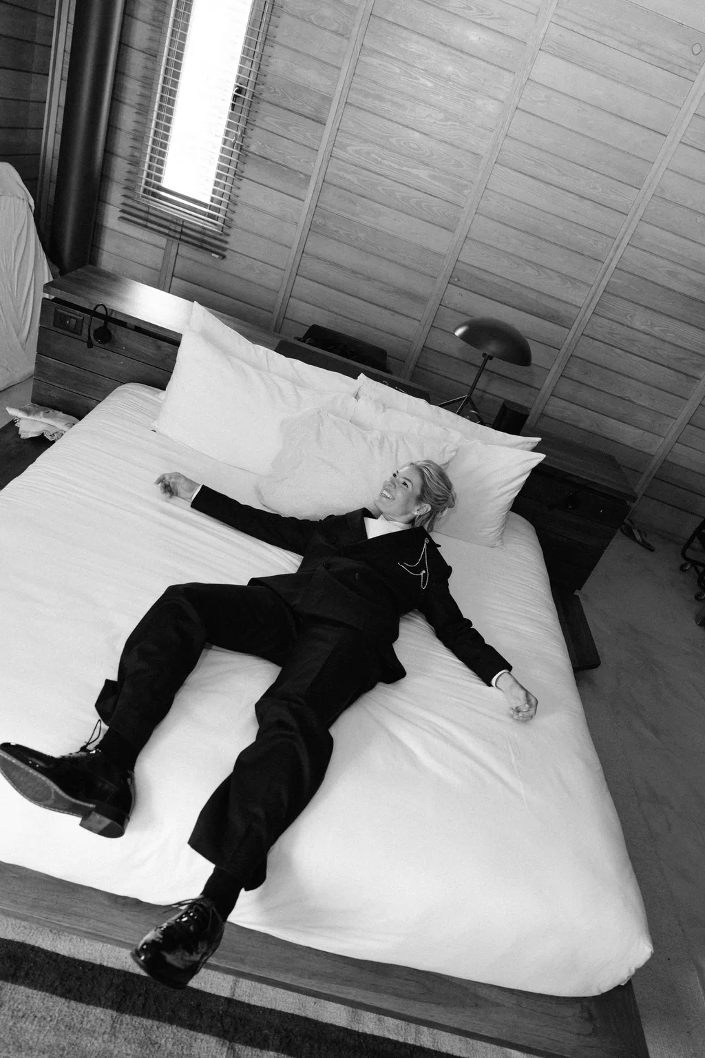 The bride in the tuxedo lying back on the bed, in black and white