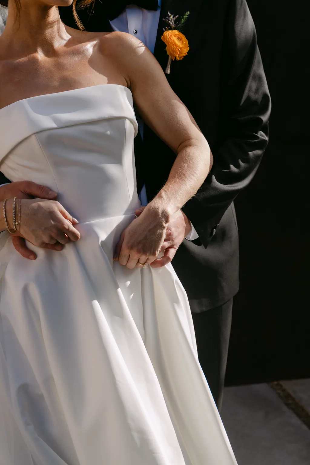 Their hands together, and the orange flower in his lapel